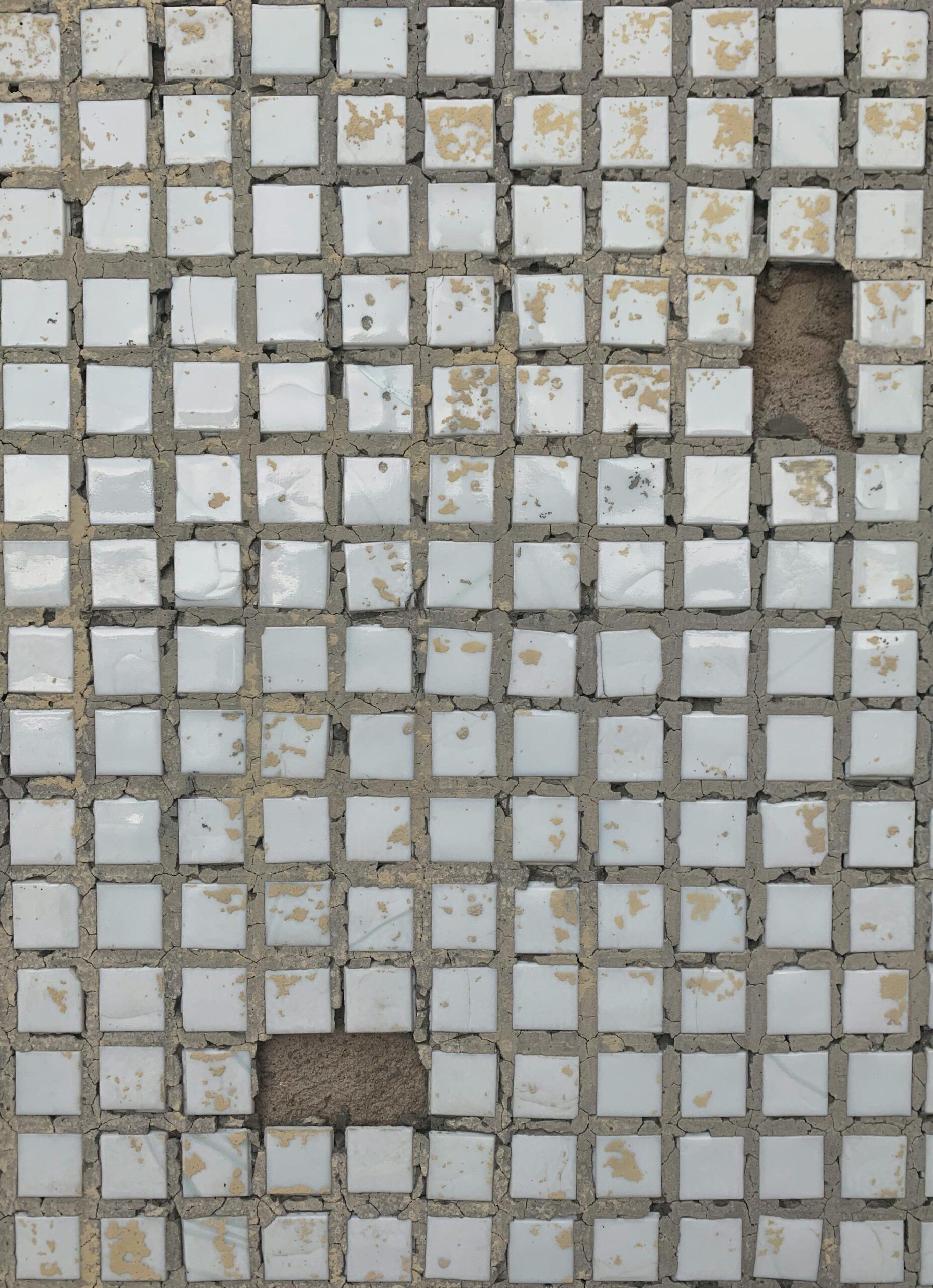 Close-up view of a worn mosaic tile pattern with missing pieces, creating an abstract texture.